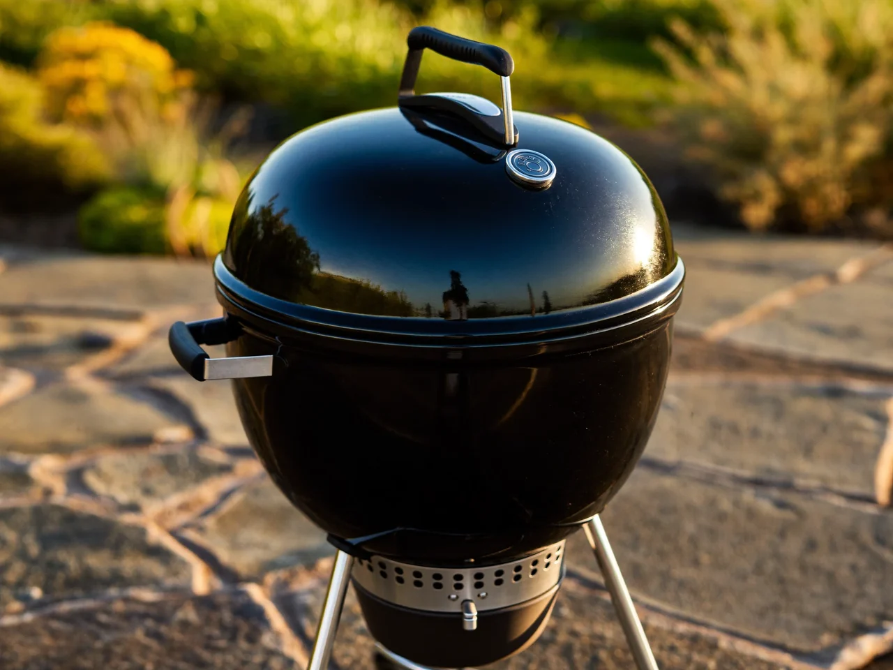 Schwarzer Kugelgrill mit gewölbtem Deckel auf einer Steinplatten-Terrasse