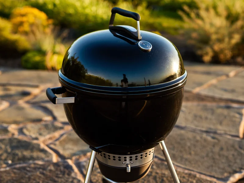 Schwarzer Kugelgrill mit gewölbtem Deckel auf einer Steinplatten-Terrasse