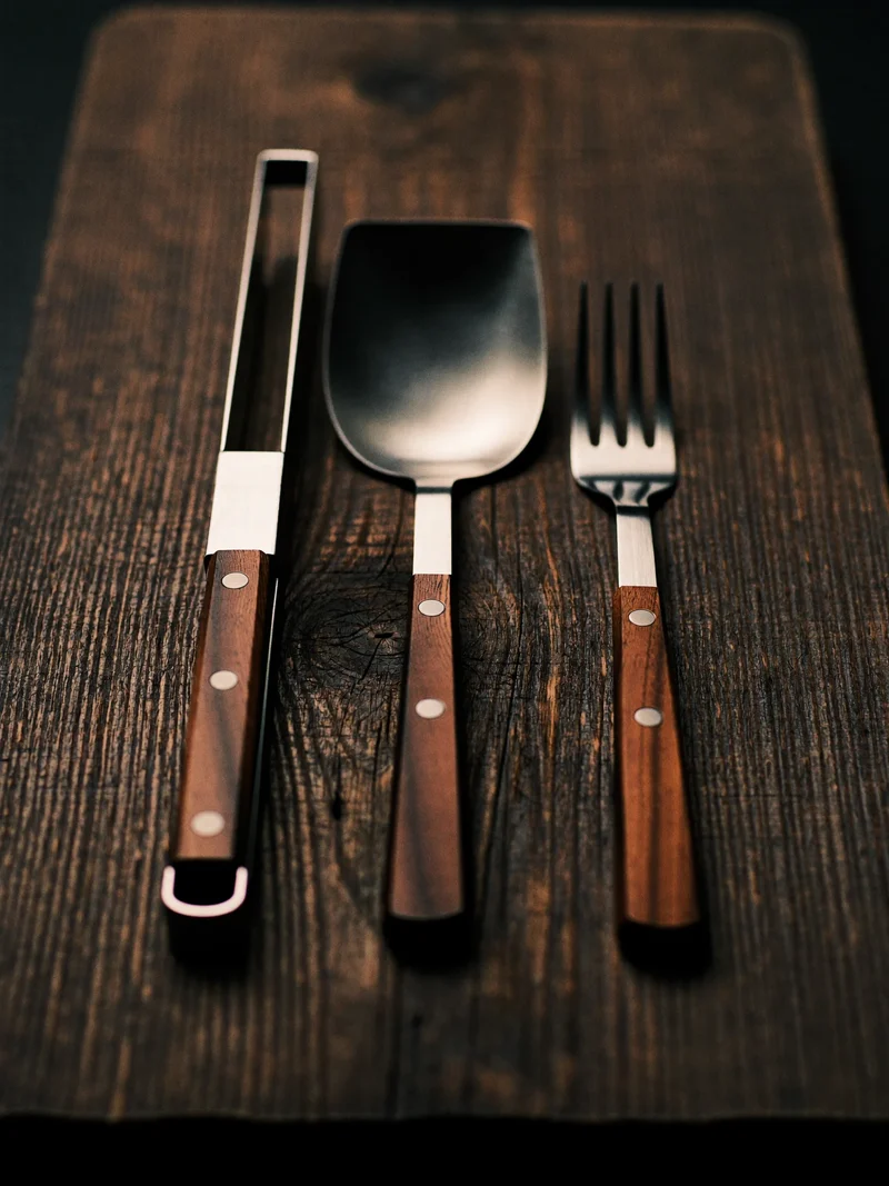 Grillzange, Wender und Gabel aus Edelstahl und Holz auf einem Holzbrett